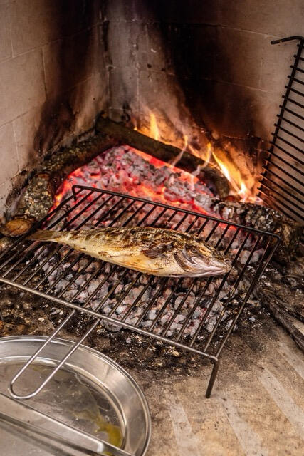 Fresh local fish cooking on the open indoor fireplace grill at Trattoria Locanda Stella in Monti, Sardinia.